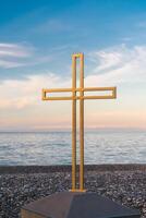 gouden kruis Aan de zee en blauw lucht. een minimalistisch visie van een gouden kruis tegen de backdrop van een bewolkt horizon. foto