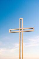gouden kruis tegen een achtergrond van blauw lucht met wolken. een minimalistisch visie van een goudkleurig kruis tegen de lucht. foto