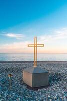 gouden kruis Aan de zee en blauw lucht. een minimalistisch visie van een gouden kruis tegen de backdrop van een bewolkt horizon. foto