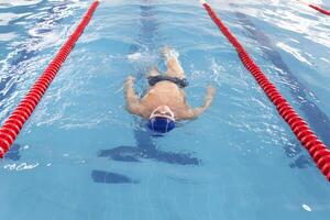 een gepensioneerde van 70 jaren rust en zwemt in de zwembad in een schoon, blauw zwembad in de vers lucht Aan vakantie. foto
