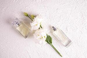 twee verschillend flessen van vrouwen parfum met een bloemen geur Aan een wit getextureerde achtergrond tussen bloemen. top visie. vlak leggen. parfum concept foto