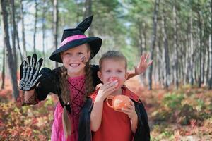 grappig kinderen in carnaval kostuums buitenshuis. een meisje gekleed net zo een heks en een jongen in een halloween kostuum laten schrikken op zoek Bij de camera. foto