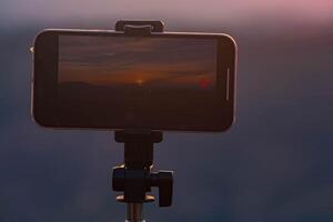 een smartphone is opname de zon instelling over- een berg bereik. foto