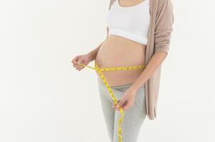 zwanger vrouw gebruik makend van meten plakband naar controleren grootte van buik zwangerschap en baby ontwikkeling foto