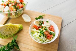 vers groente salade, kool, tomaten in een kom Aan een houten tafel foto