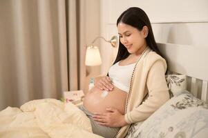 mooi zwanger vrouw toepassen hydraterend, rekken Mark room Aan buik, vruchtbaarheid onvruchtbaarheid behandeling, ivf, toekomst moederschap concept foto