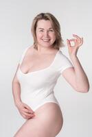 geluk plus grootte vrouw in bodysuit shows OK teken. uitgebreid maten model- lachend, op zoek Bij camera foto