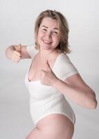 portret plus grootte vrouw in bodysuit tonen duimen omhoog, glimlachen en vangt essence lichaam positief foto