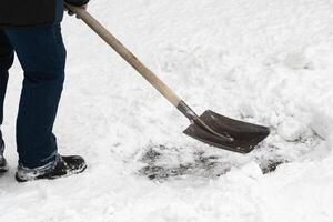 een onherkenbaar arbeider is Verwijderen sneeuw met een ijzer Schep met een houten omgaan met na een sneeuwval foto