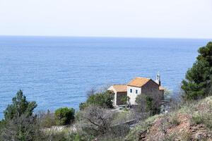 klokken Aan een steen klooster met een oranje dak tegen een backdrop van zee en bergen. klooster bovenstaand sveti stefan in Montenegro. egorova pad. horizontaal. foto