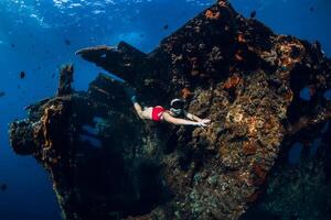 vrouw freediver glijdt met vinnen Bij wrak schip. gratis duiken in blauw oceaan in de buurt wrak foto