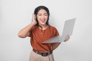 gelukkig jong vrouw vervelend bruin overhemd en koptelefoon terwijl Holding laptop naar luister muziek- geïsoleerd over- wit achtergrond. foto