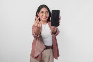 schattig Aziatisch bedrijf vrouw in bril presenteren kopiëren ruimte Aan haar telefoon scherm terwijl maken vinger hart vorm geven aan, geïsoleerd door wit achtergrond. foto