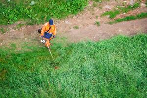 een Mens maait de hoog gras met een trimmer foto