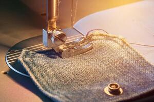 voet van naaien machine Aan jeans kleding stof, warm licht foto