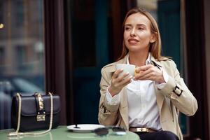 elegant jong vrouw drinken koffie Aan restaurant terras en op zoek Bij kant foto