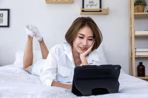 jong mooi meisje werken van huis Aan haar bed gebruik makend van digitaal tablet naar toegang haar bedrijf werk voor onderwijs studie en online dating foto