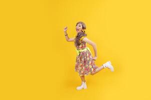 Aziatisch hippie vrouw jurk in 80s wijnoogst mode met kleurrijk retro kleding terwijl dansen en rennen geïsoleerd Aan geel achtergrond voor luxe kleding partij en knal cultuur concept foto