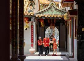 Aziatisch familie met senior ouder in rood cheongsam qipao jurk is helpen de opa naar wandelen in de tempel naar betalen hulde naar Voorouder gedurende Chinese maan- nieuw jaar in hun geboorteplaats foto