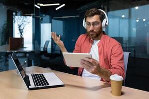 Mens met hoofdtelefoons en tablet computer Bij werkplaats teleurgesteld met spel resultaat, zakenman programmeur aan het kijken online sport- bij elkaar passen en juichen. foto