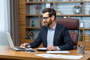 geslaagd financier investeerder werken met documenten en rekeningen binnen kantoor, zakenman met baard glimlachen tevreden met werk resultaten en prestaties, Mens binnen kantoor met laptop werken. foto