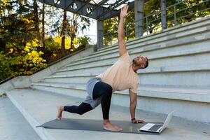 Afrikaanse Amerikaans mannetje sportman trainer opleiding online via laptop Bij stadion. shows opdrachten, strekt zich uit, yoga Aan de mat. foto