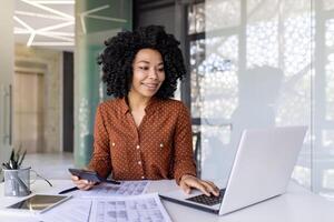 geslaagd gelukkig accountant financier met een rekenmachine bereidt zich voor een financieel verslag doen van en vult in tafel vormen, zakenvrouw werken met papieren, contracten binnen kantoor, vrouw arbeider met een laptop. foto