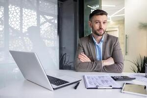 echt, gefocust financier accountant Aan papier werk binnen kantoor, volwassen Mens gebruik makend van rekenmachine en laptop voor berekenen rapporten en samenvatten rekeningen, zakenman Bij werk op zoek camera foto