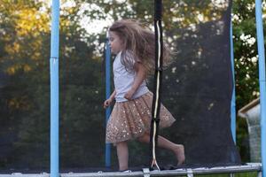 weinig kind meisje jumping Aan de trampoline in de terug werf foto