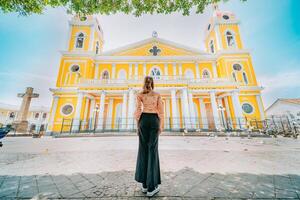 achterzijde visie van een toerist vrouw in voorkant van een kathedraal in een toerist vierkant. terug visie van een mooi toerist in de toerist plein van granada, Nicaragua foto