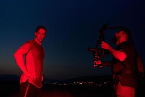 's nachts vastleggen. professioneel videograaf films atleten rennen in rood verlicht duisternis foto