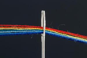 veelkleurig draden voor naaien in de het formulier van een regenboog voorbij gaan aan door een antiek naald- Aan een zwart achtergrond foto