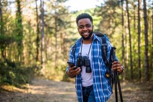 jong Mens geniet wandelen en gebruik makend van mobiel telefoon in natuur. foto