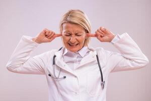 portret van overwerkt volwassen vrouw dokter met handen in oren geschreeuw Aan grijs achtergrond. foto