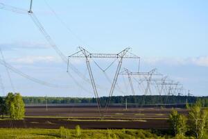 een hoog voltage macht lijn Aan de achtergrond van een landelijk veld. landschap in de dorp en elektrisch bedrading. foto