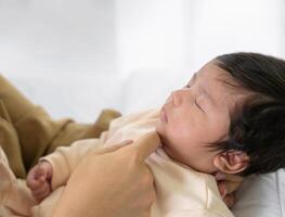 moeder hand- aanraken kin van pasgeboren baby dochter Aan bed Bij huis. zuigeling meisje of jongen slapen Aan mam arm. liefde en nieuw leven concept foto