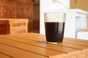 glas kop gevulde met zwart koffie Aan een bruin tafel foto