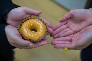 hand- geven heerlijk geglazuurd donut met subtiel naar vriend foto