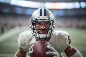 Amerikaans Amerikaans voetbal speler in een grijs helm en wit uniform met een bal in zijn handen. Aan de achtergrond van de Amerikaans voetbal veld- en de staat van de arena foto