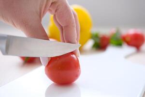 vrouw snijdend uien en groenten Aan snijdend bord detailopname van vrouw handen snijden kers tomaat met mes Aan houten bord, Koken groente salade foto
