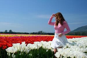 mooi jong meisje in wit tulpen staat glimlachen past zich aan haar haar- tegen de lucht bergen wit tennis rok roze blouse ruimte voor tekst voorjaar schoonheid jeugd licht foto