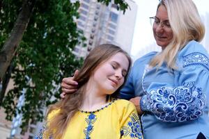 moeder en dochter in geborduurd overhemden blauw en geel blouse schattig familie verhouding detailopname portret gezicht buitenshuis gelukkig senior vrouw genieten van in van dochter genegenheid Aan moeder dag. foto