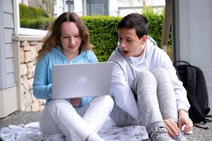 online opleiding jongens meisje in de buurt laptop jongen geopend mond looks in apparaatje nieuw film project beoordeling van oplossing van probleem interessant tijdverdrijf jongen veters omhoog sneaker De volgende naar rugzak school- vrienden foto