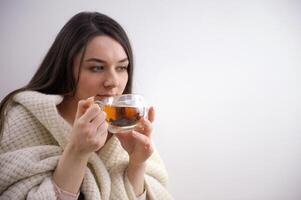 portret van blij jong vrouw genieten van een kop van koffie Bij huis. glimlachen mooi meisje drinken heet thee in winter. opgewonden vrouw vervelend bril en trui en lachend in een herfst dag. foto