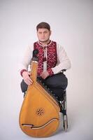 oekraïens Kozakken Speel harp knap jong Mens met kobza musical instrument in handen zit Aan wit achtergrond oorlog veteraan gekleed in oekraïens geborduurd overhemd nationaal symbolen van Oekraïne vyshyvanka foto