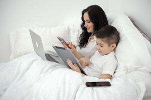 werk Bij huis online mam en zoon zitten in bed laptop tablet telefoon lessen online werk vrouw pratend telefoon glimlachen maken bestellen lost op bedrijf problemen intimiteit liefde single moeder werk is uit van de kantoor foto