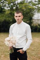 een Mens in een wit overhemd en zwart broek is Holding een boeket van bloemen foto