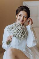 een vrouw is zittend Aan een stoel en Holding een boeket van wit bloemen foto