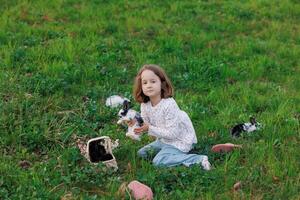 een jong meisje is zittend in een met gras begroeid veld- Holding een konijn foto