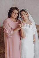 een moeder knuffels haar dochter, de bruid, vervelend een bruiloft jurk foto